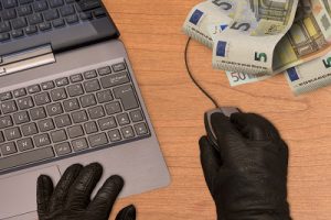 Computer crime metaphor, hand in black gloves with mouse, computer and banknotes.